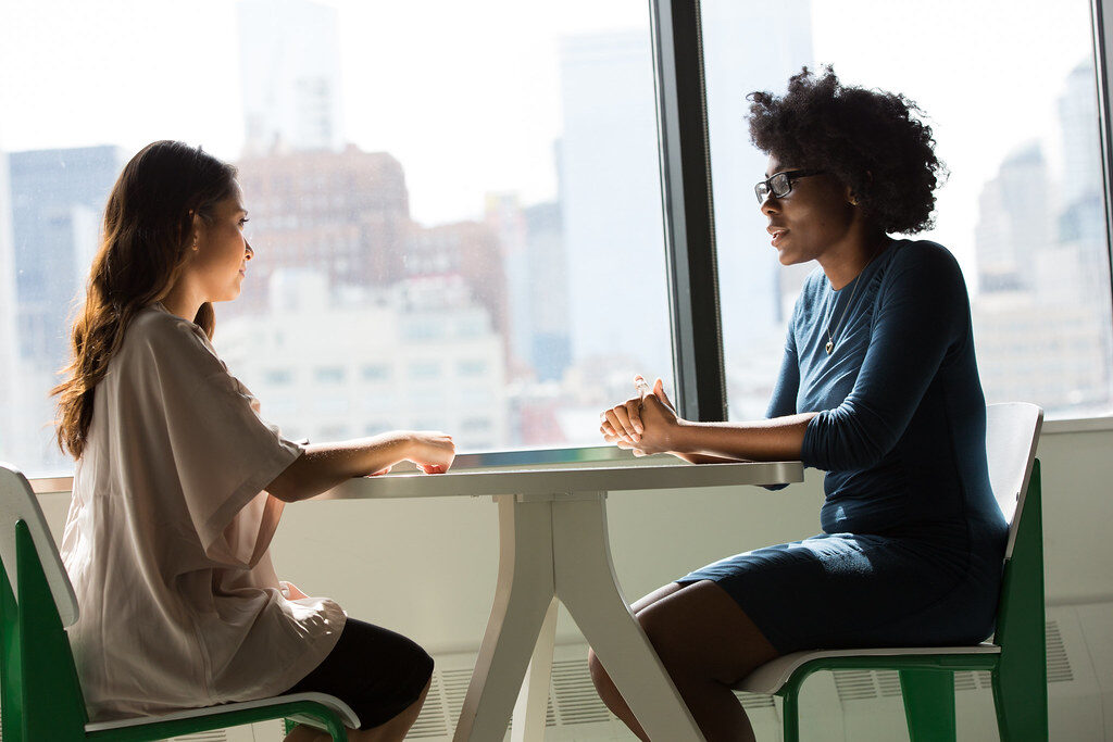 Two learners discussing their work at a table by the window